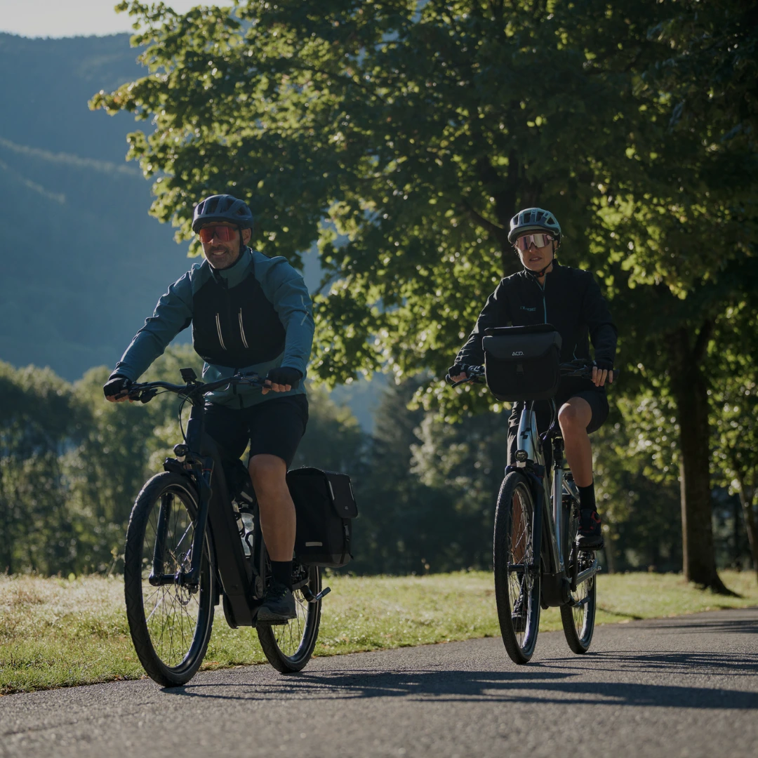 E-Bike Hardtail Zwei Radfahrer fahren entspannt auf einem sonnigen Landweg mit Ausblick auf die Berge