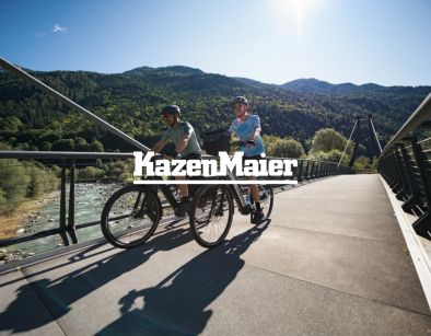 Kazenmaier Leasing Logo auf Hintergrund mit zwei Radfahrern die über eine Brücke fahren